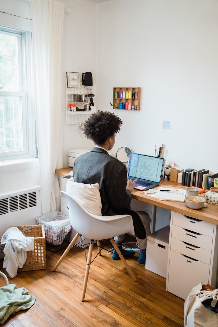 A person working remotely at a home office desk with a laptop and organized workspace.